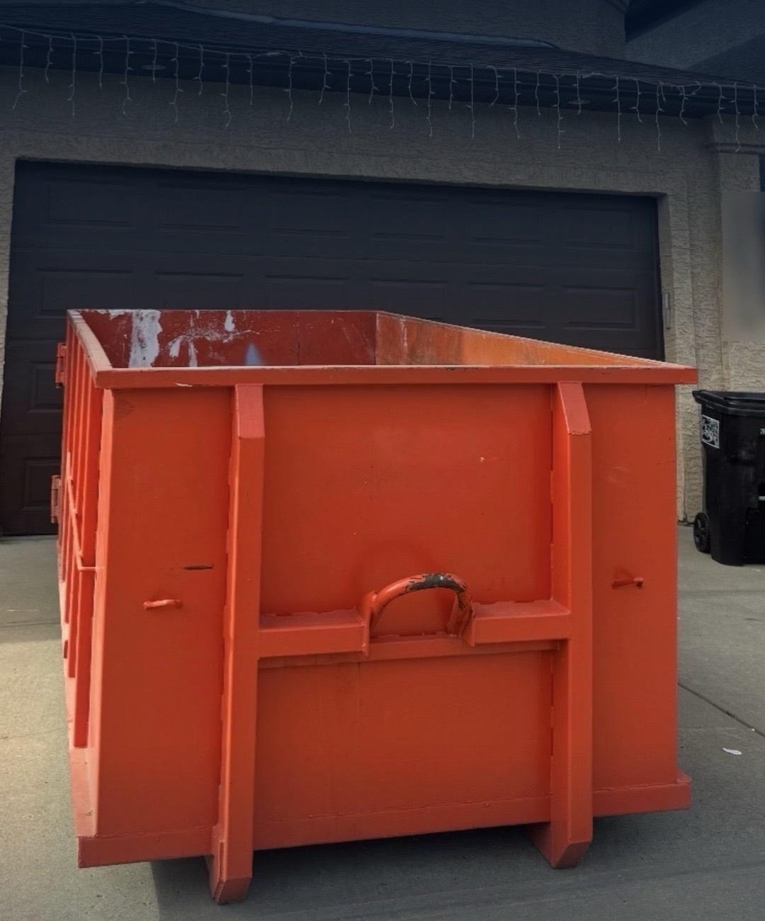 Orange Hauling Heroes bin placed on a residential driveway in front of a garage