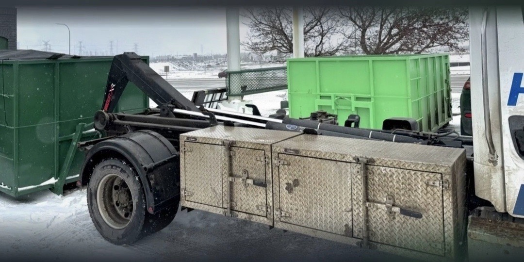 Side view of the Hauling Heroes hook-lift truck beside green bins