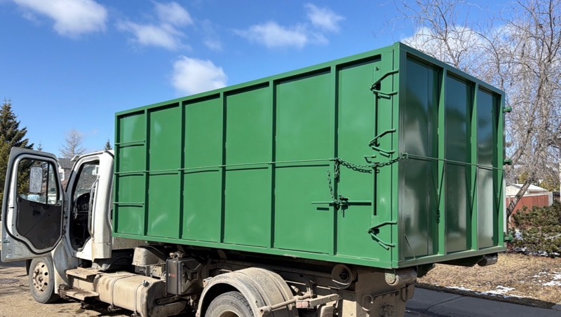 Hauling Heroes hook-lift truck carrying a green roll-off bin on a residential street