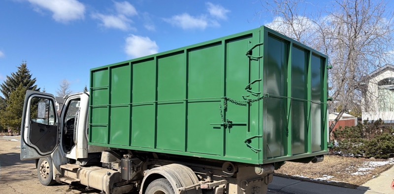 Hauling Heroes hook-lift truck carrying a green roll-off bin on a residential street