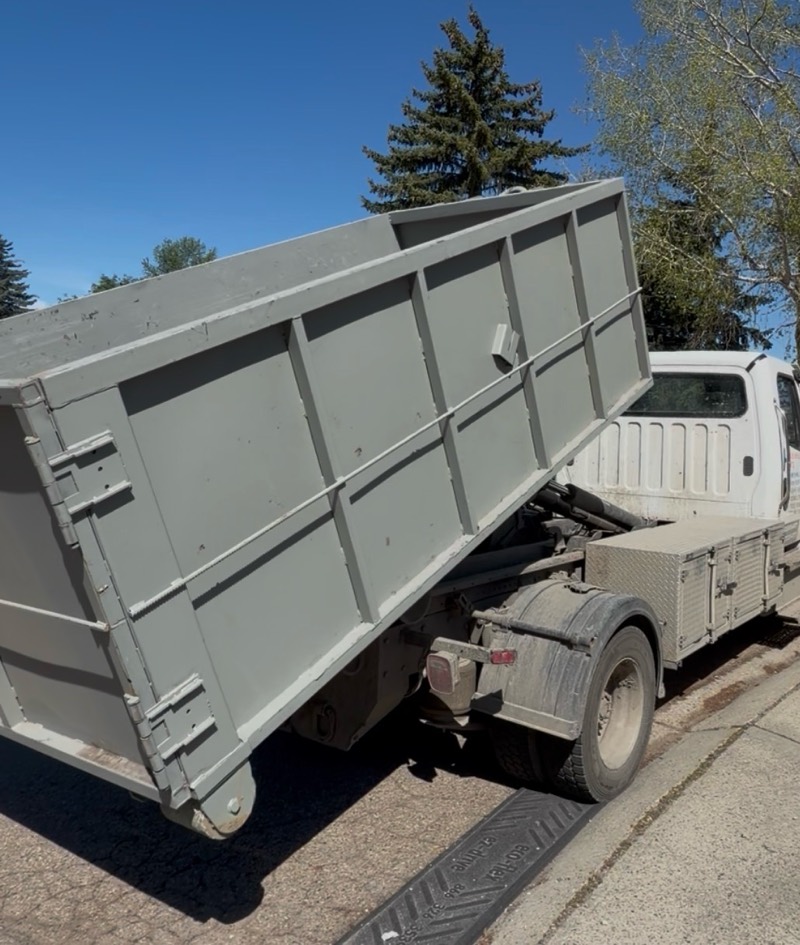 Hauling Heroes truck tipping a grey roll-off bin into place at the curb