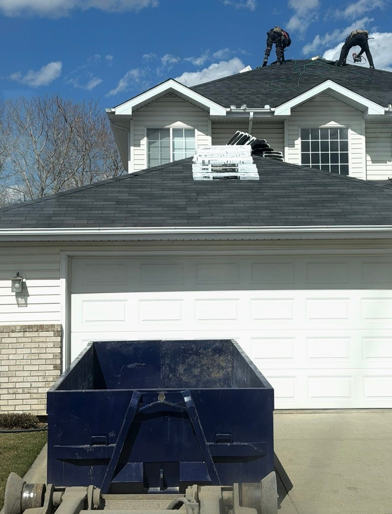 Navy Hauling Heroes roll-off bin on a residential driveway in front of a garage during a roof replacement