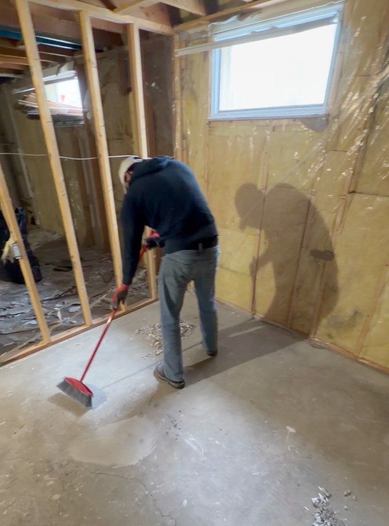 Crew member sweeping a basement floor after the interior was stripped back to the framing