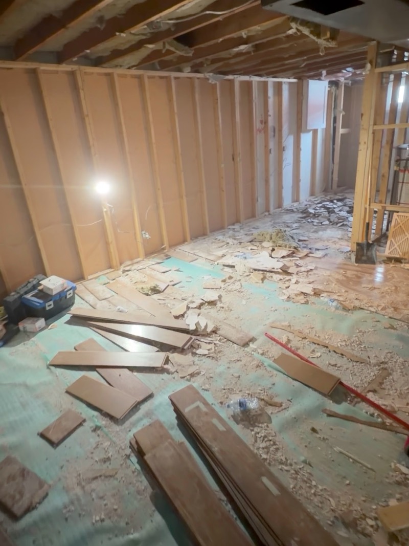 Basement stripped back to the wall framing, with removed flooring pieces on the floor