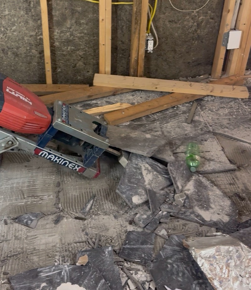 Broken concrete slab pieces beside a jackhammer trolley in an unfinished basement