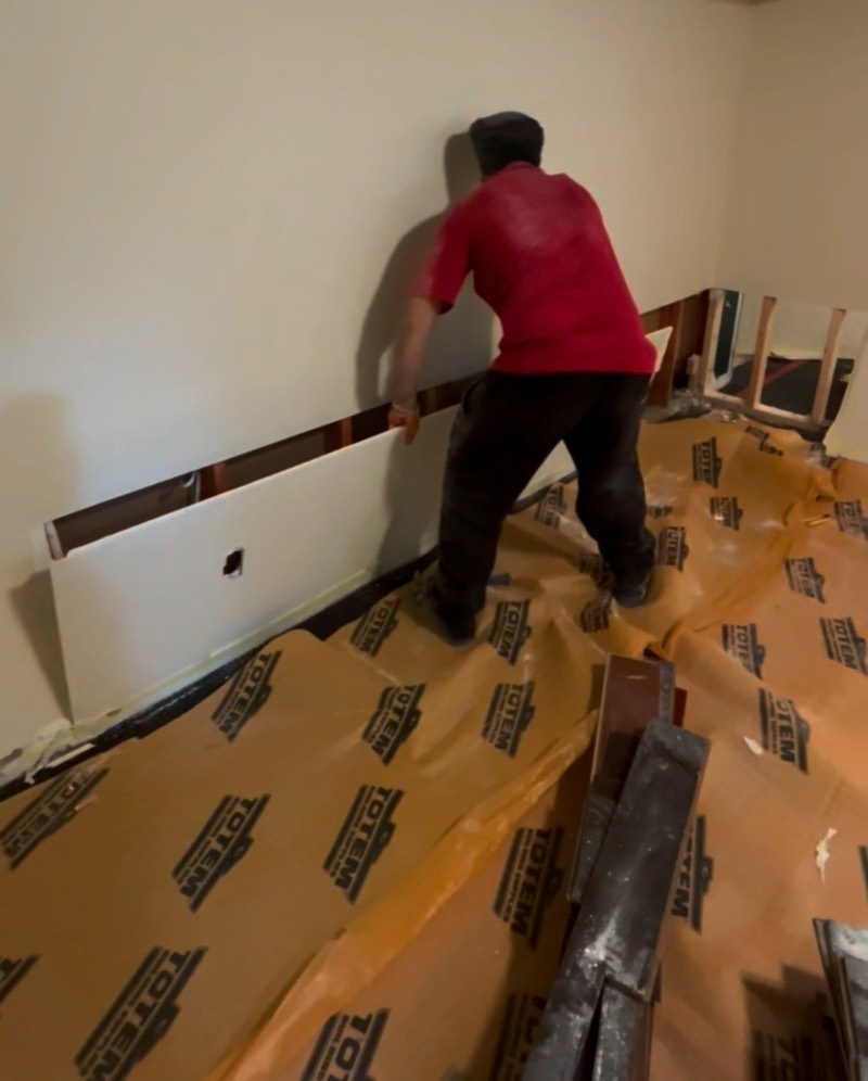 Crew member removing a lower section of drywall, with protective board laid over the floor