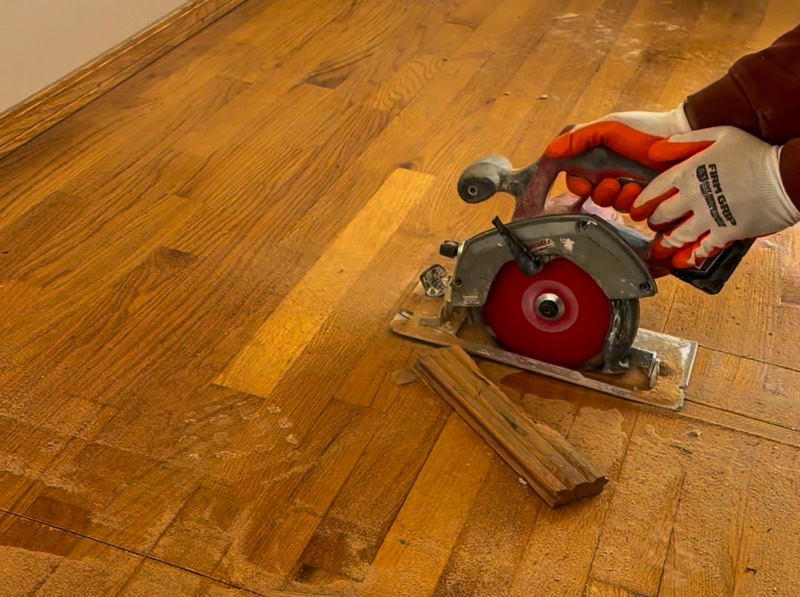 Crew member cutting through hardwood flooring with a circular saw during interior demolition