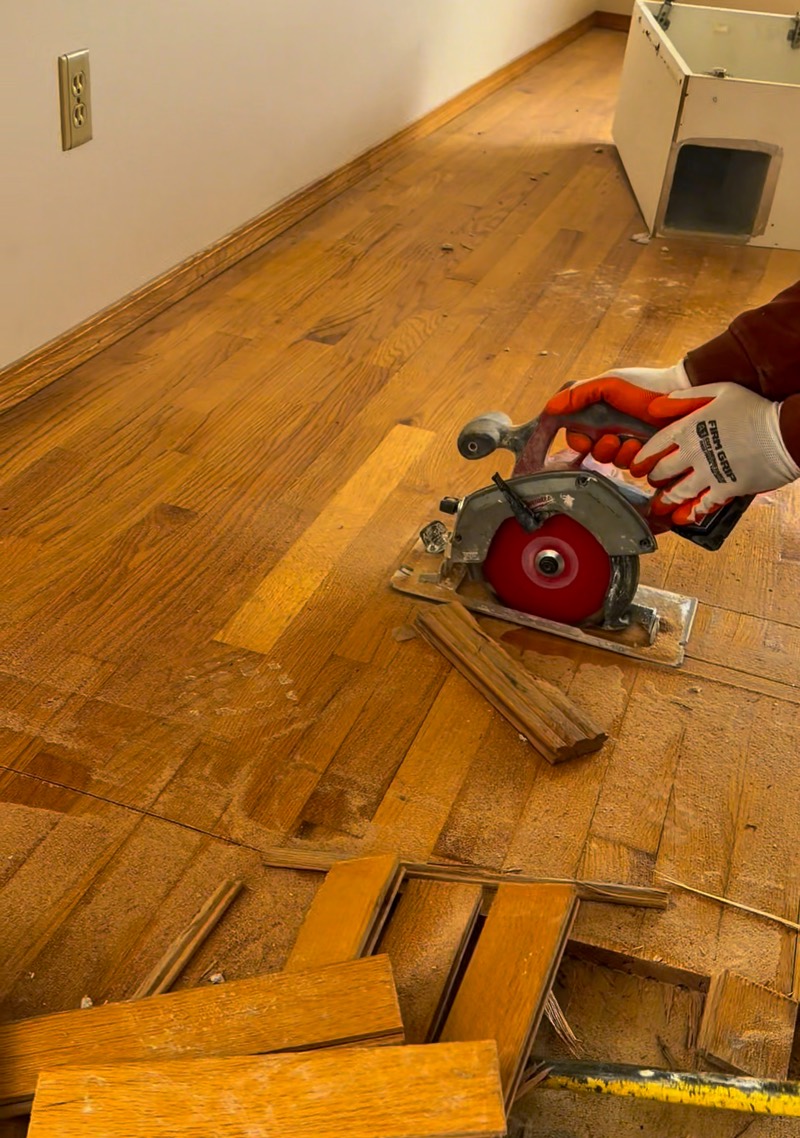 Crew member cutting through hardwood flooring with a circular saw during interior demolition