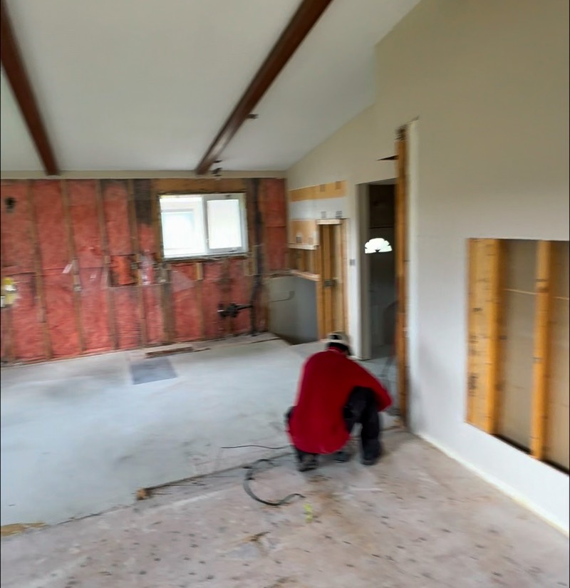 Room stripped back to the insulation and studs, with a crew member working on the floor