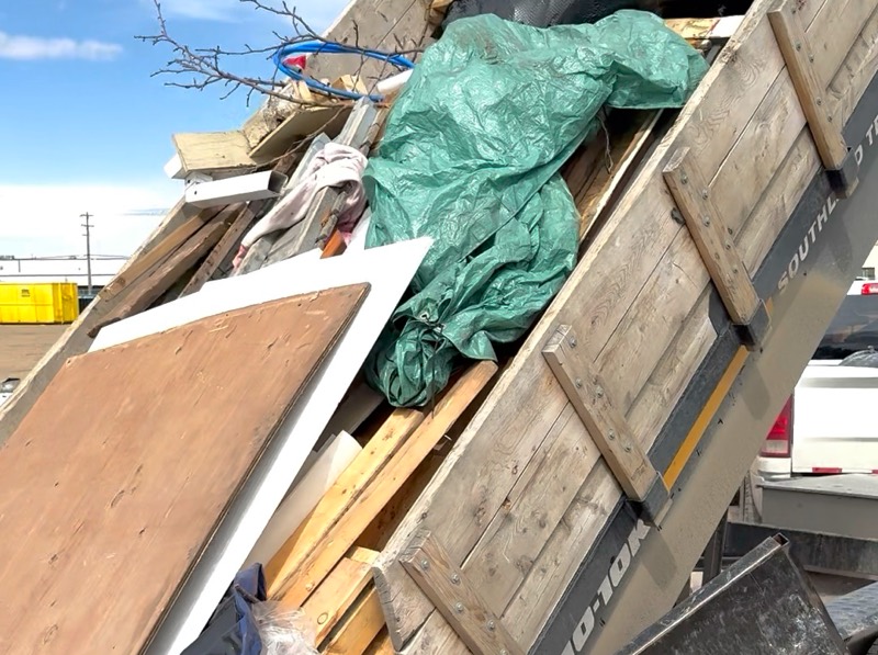 Dump trailer tipping a full load of lumber, plywood and bagged junk