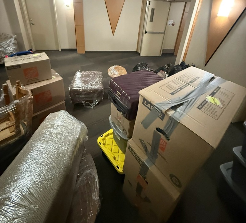 Boxes, suitcases and a plastic-wrapped rug staged in an apartment hallway before loading