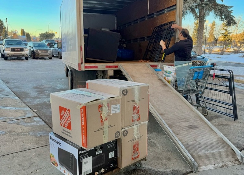 Mover loading a box truck by ramp, with boxed appliances on a dolly in the foreground