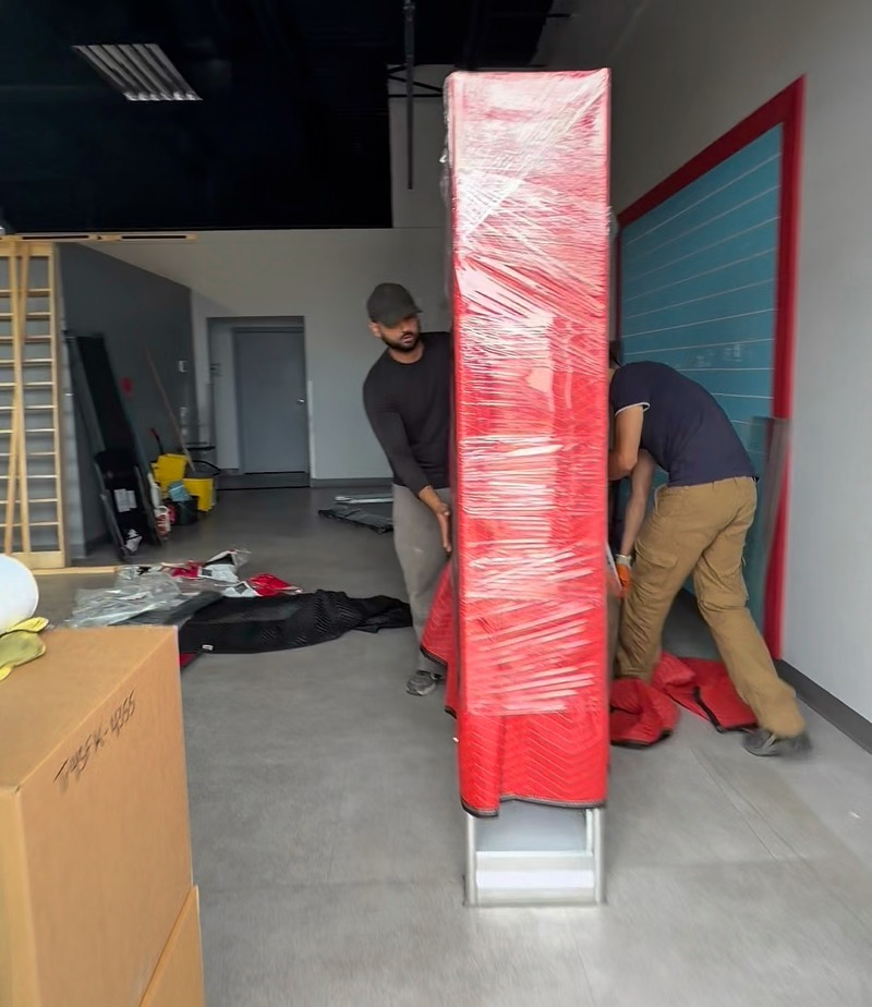 Crew wrapping a tall cabinet in red stretch wrap during a commercial move