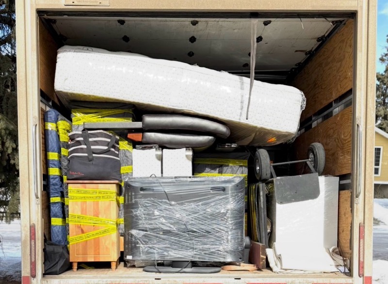 Back of a moving truck packed with a wrapped mattress and shrink-wrapped furniture