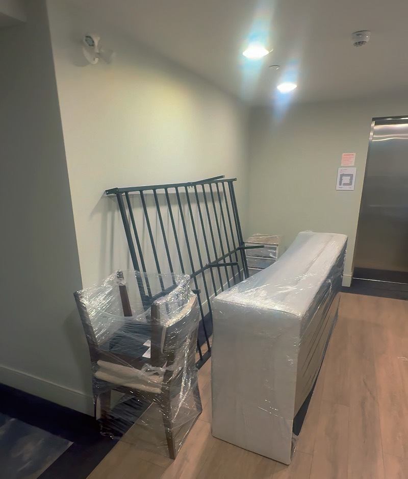Shrink-wrapped chairs and a padded, plastic-wrapped sofa staged in an apartment hallway for a move